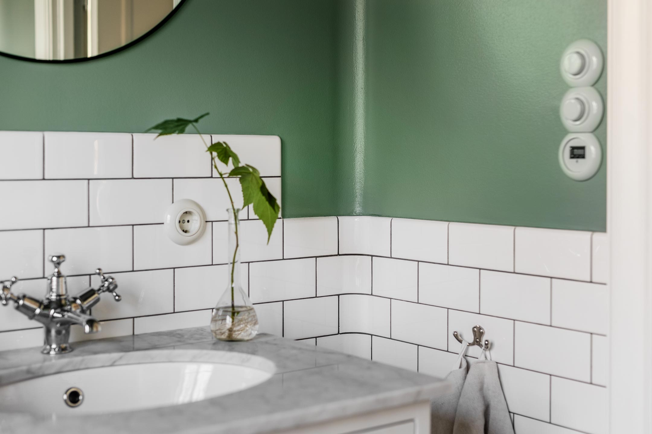 Badeværelse med hvide rektangulære fliser, grønmalet væg og porcelænsafbrydere Badeværelse med hvide rektangulære fliser, grønmalet væg og porcelænsafbrydere