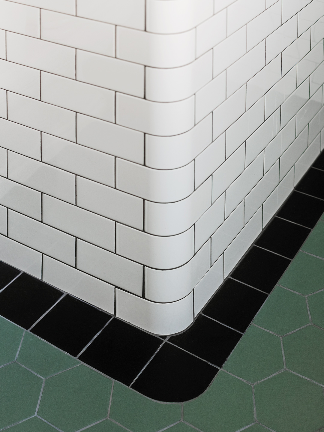 Detalje af hjørne med hvide fliser, sort klinkerkant og grønne gulvklinker Detalje af hjørne med hvide fliser, sort klinkerkant og grønne gulvklinker