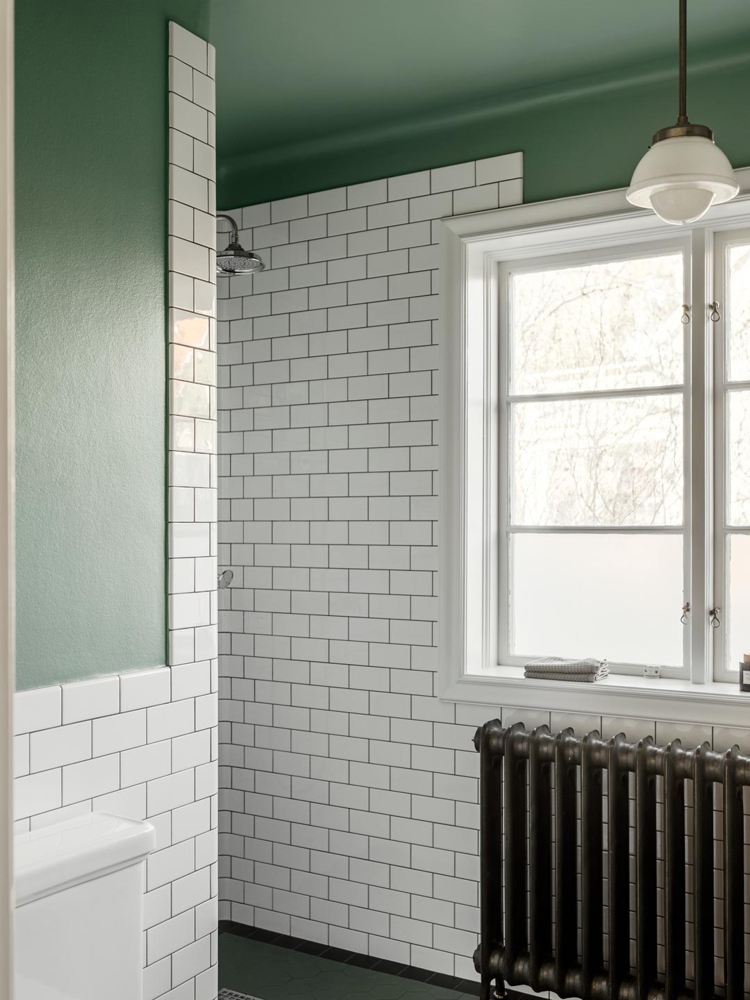 Badeværelse med grønne vægge, hvide metrofliser, sort radiator og bruser Badeværelse med grønne vægge, hvide metrofliser, sort radiator og bruser