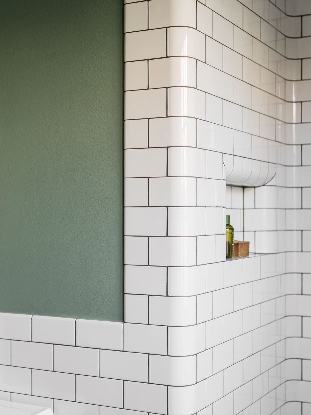 Detalje af badeværelse med grøn væg, hvide fliser og indbygget niche Detalje af badeværelse med grøn væg, hvide fliser og indbygget niche