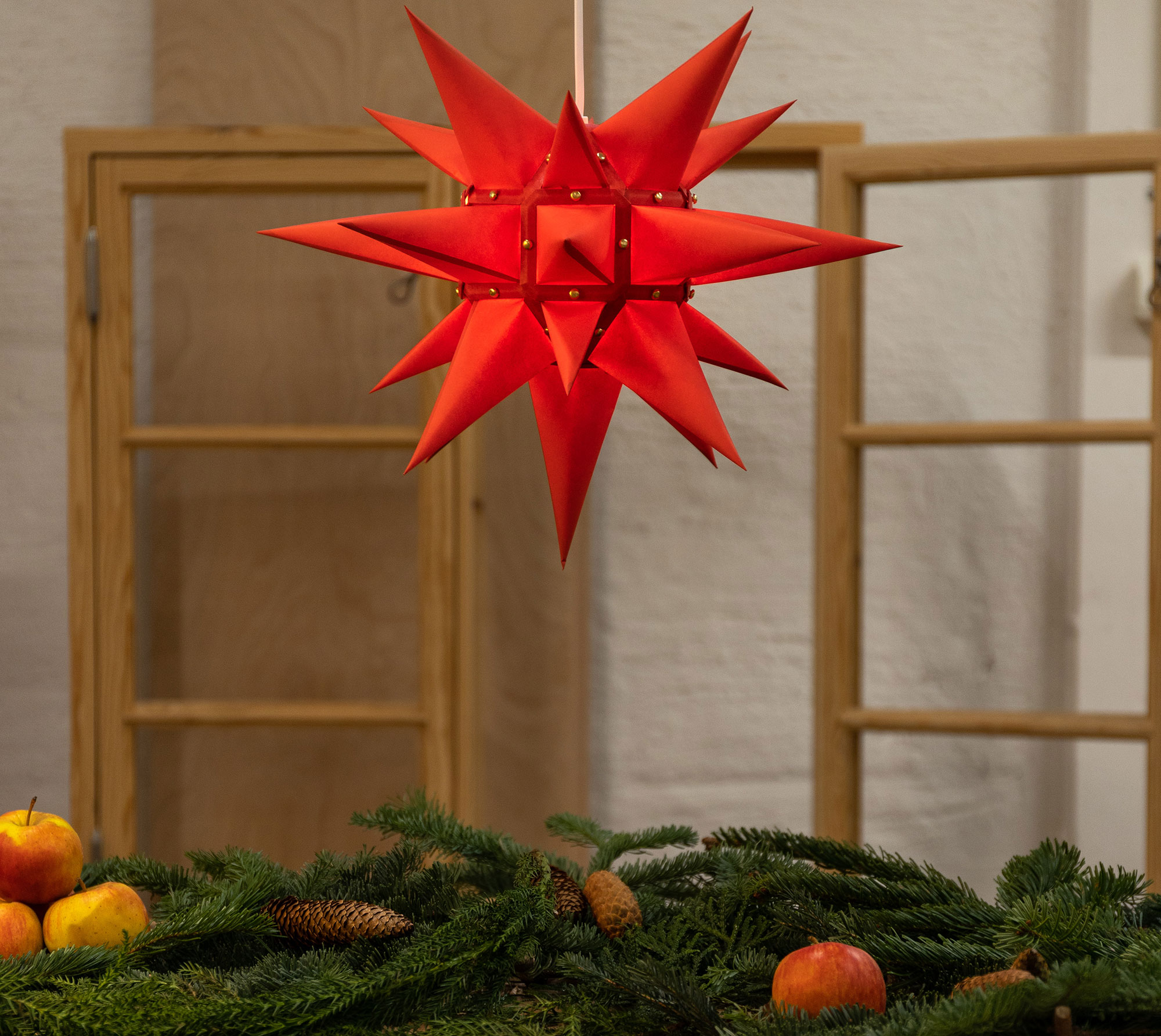 Herrnhuterstjerne i rød som julepynt, hængende over gran, kogler og æbler i klassisk juledekoration. Herrnhuterstjerne i rød som julepynt, hængende over gran, kogler og æbler i klassisk juledekoration.