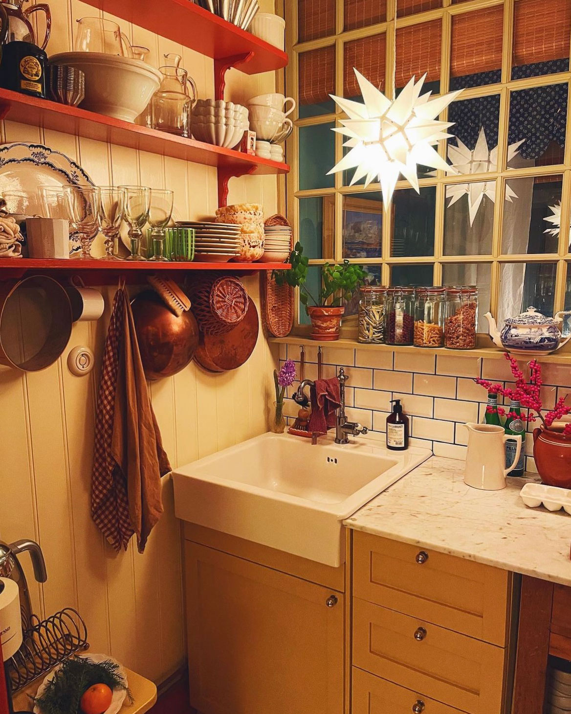 Herrnhuterstjerne som julelampe over køkkenbord med gule skabe, hylder med service og julestemning. Herrnhuterstjerne som julelampe over køkkenbord med gule skabe, hylder med service og julestemning.