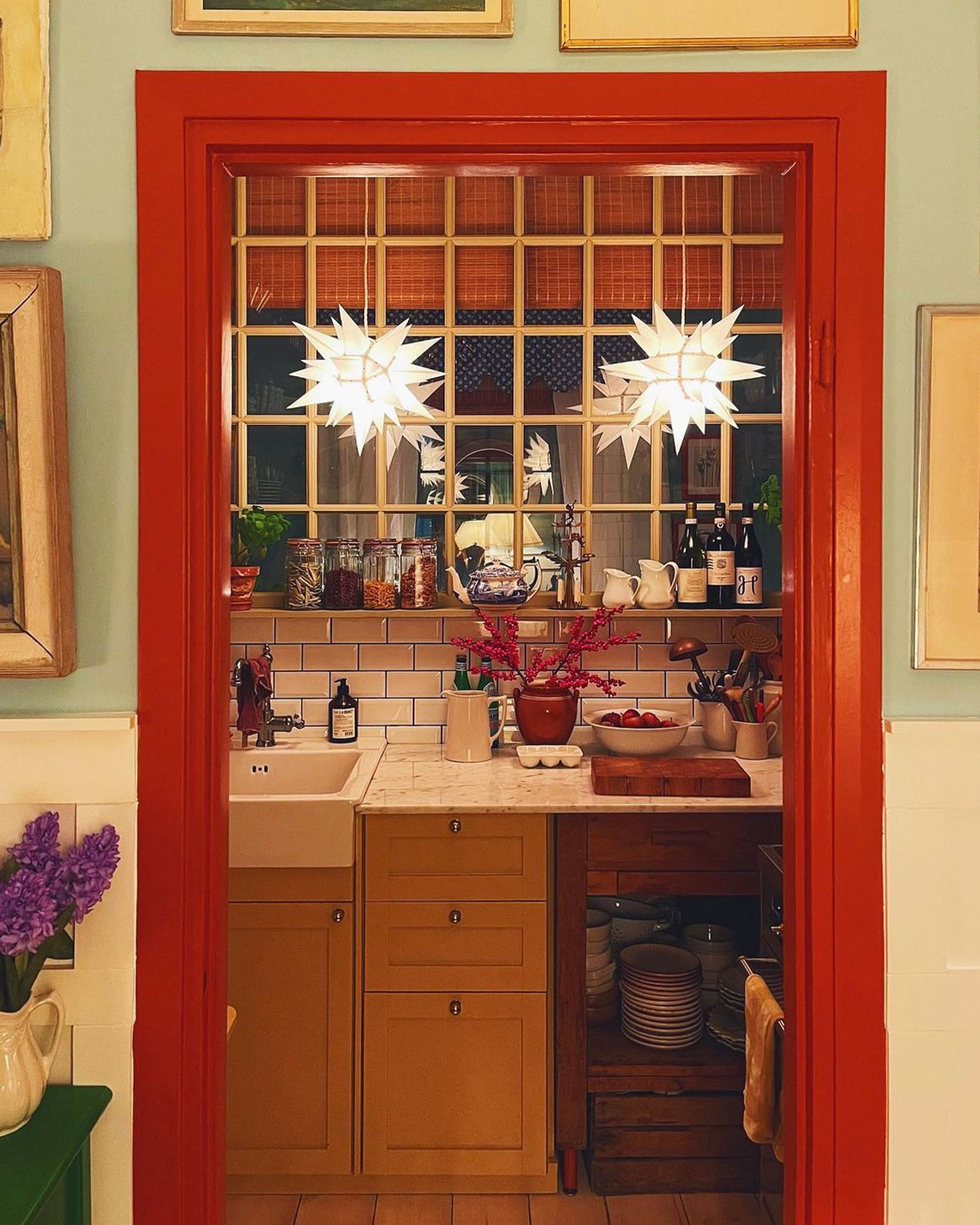 To Herrnhuterstjerner som julestjerner i køkkenvindue, set gennem rødt dørkarme og klassisk indretning. To Herrnhuterstjerner som julestjerner i køkkenvindue, set gennem rødt dørkarme og klassisk indretning.