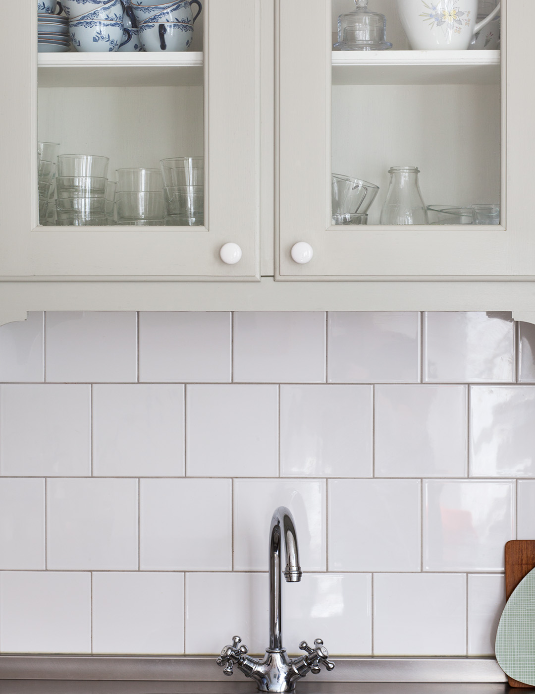 Specialbygget k&oslash;kken i 1920&rsquo;er-stil malet i en lys gr&aring;gr&oslash;n linoliemaling. L&aring;gerne har indfattet glas, og v&aelig;ggen er bekl&aelig;dt med hvide kvadratiske kakelfliser.
