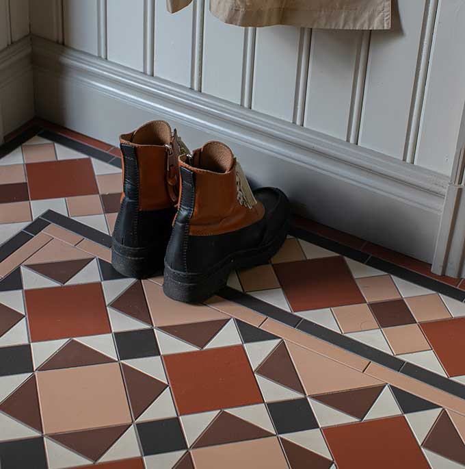 Inspirationsbild Victorian floor tiles i fem kulörer Mönstrat klinkergolv med flera olika former i bruna, röda och vita toner mot pärlspontspanel i grått.
